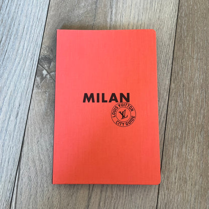 Louis Vuitton *Milan* City Guide is an English-language travel guide with a cloth-bound hardcover. It features recommendations for hotels, restaurants, museums, shopping, and cultural attractions throughout Milan. The edition includes guest contributions by Mahmood, writing by Pierre Léonforte, Corrado Beldi, Katia Kulawick-Assante, and Isabelle Valembras Dahirel, along with exclusive photography by Denis Bourges.
