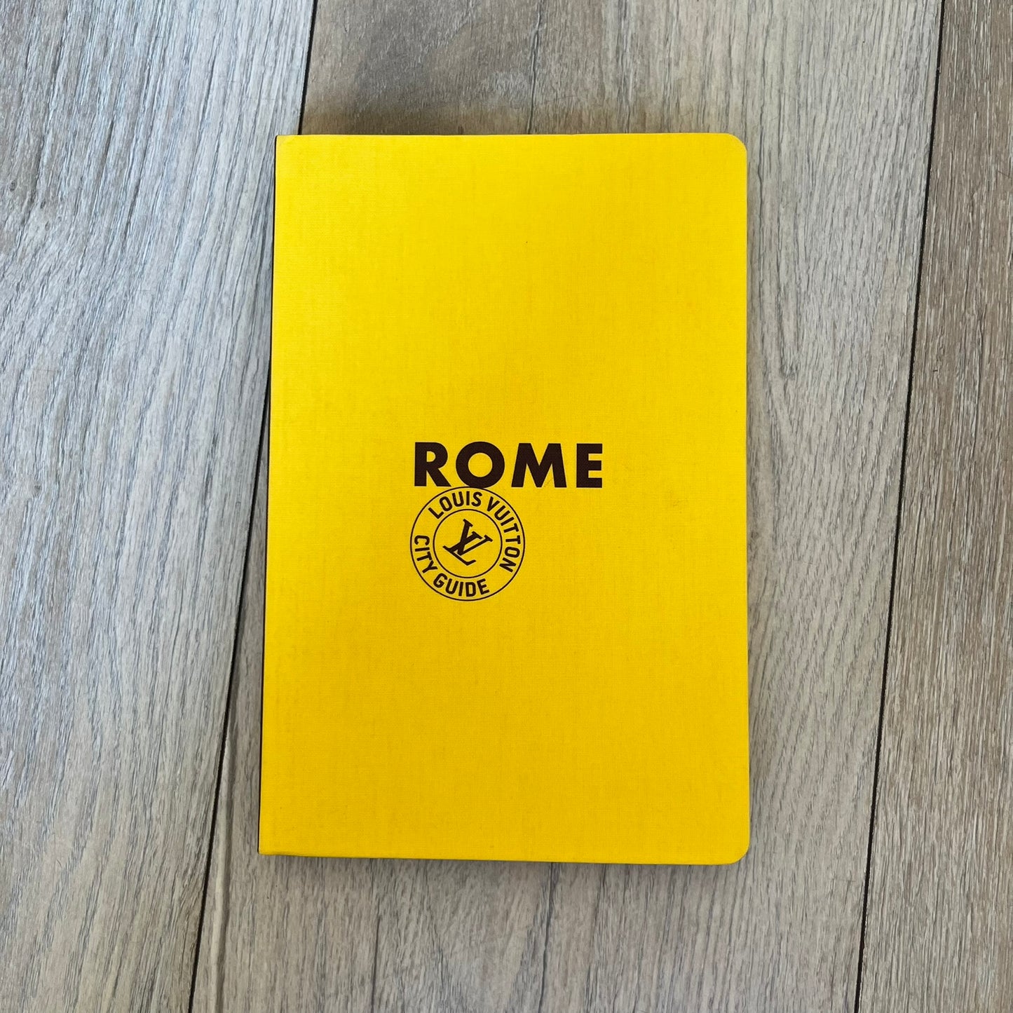 Louis Vuitton Rome City Guide is an English-language travel guide with a cloth-bound hardcover. It features recommendations for hotels, restaurants, museums, shopping, and cultural attractions throughout Rome. The edition includes guest contributions by Sam Stourdzé, writing by Pierre Léonforte, Isabelle Sciamma, and Marc-Henri Maisonhaute, along with exclusive photography by Gilles Coulon.