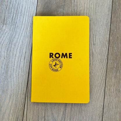 Louis Vuitton Rome City Guide is an English-language travel guide with a cloth-bound hardcover. It features recommendations for hotels, restaurants, museums, shopping, and cultural attractions throughout Rome. The edition includes guest contributions by Sam Stourdzé, writing by Pierre Léonforte, Isabelle Sciamma, and Marc-Henri Maisonhaute, along with exclusive photography by Gilles Coulon.