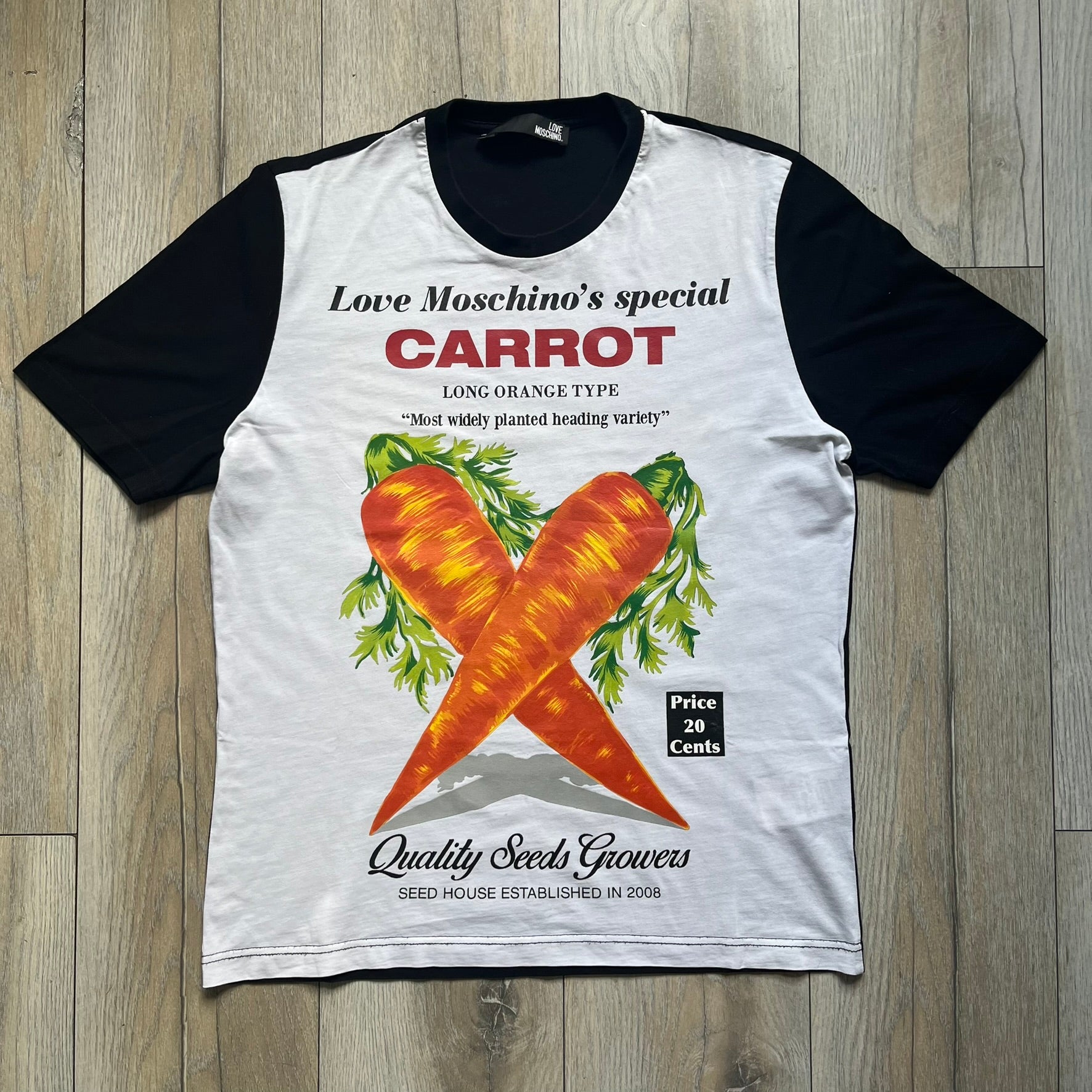 Love Moschino 2010s Carrot Tee is a black and white T-shirt with black sleeves and back panel. The front features Love Moschino branding above two illustrated carrots, with large red “CARROT” text underneath and “Price 20 Cents” text below. The front graphic is designed in the style of a vintage carrot advertisement.
