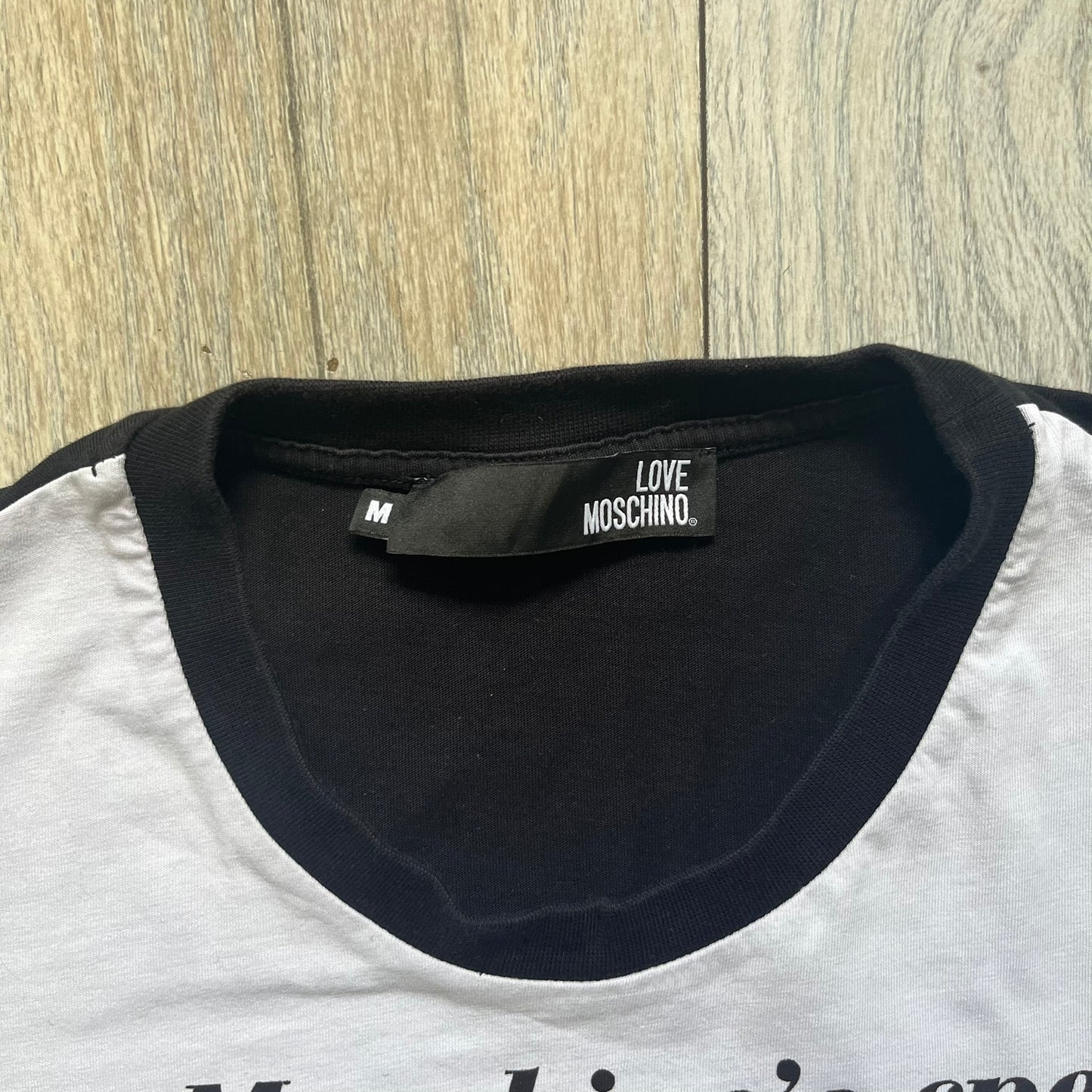 Love Moschino 2010s Carrot Tee is a black and white T-shirt with black sleeves and back panel. The front features Love Moschino branding above two illustrated carrots, with large red “CARROT” text underneath and “Price 20 Cents” text below. The front graphic is designed in the style of a vintage carrot advertisement.
