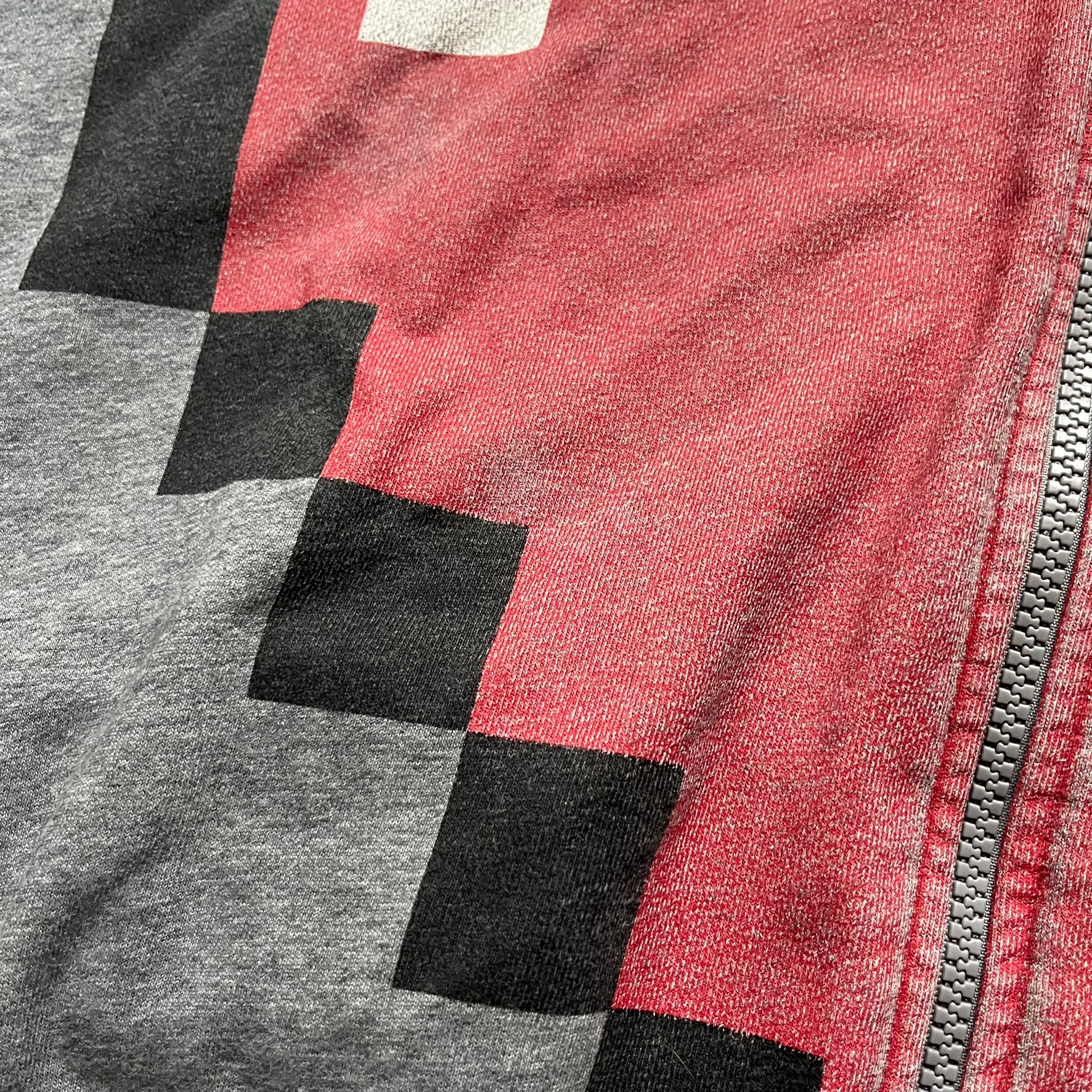 Love Moschino Pixel Heart Gray Hoodie is a gray zip-up hoodie featuring a large red pixel heart graphic on the front. It has slightly shorter-than-standard sleeves, long drawstrings, and a front zipper closure. The lower part includes Love Moschino logo detailing, completing the branded design.
