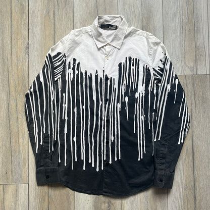 Love Moschino SS19 Dripping Paint Print Button-Up Shirt is a black and white shirt from the Spring/Summer 2019 collection. The upper portion is white, while the lower portion is black. The transition between the two sections features a dripping paint graphic extending downward from both sides into the black area. The button closure uses matching buttons, with white buttons on the white section and black buttons on the black section.
