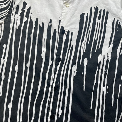 Love Moschino SS19 Dripping Paint Print Button-Up Shirt is a black and white shirt from the Spring/Summer 2019 collection. The upper portion is white, while the lower portion is black. The transition between the two sections features a dripping paint graphic extending downward from both sides into the black area. The button closure uses matching buttons, with white buttons on the white section and black buttons on the black section.
