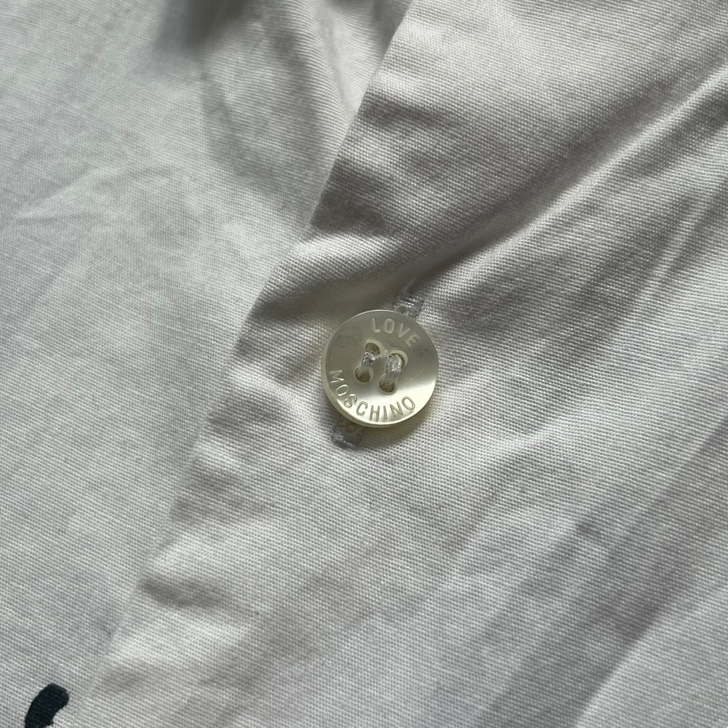 Love Moschino SS19 Dripping Paint Print Button-Up Shirt is a black and white shirt from the Spring/Summer 2019 collection. The upper portion is white, while the lower portion is black. The transition between the two sections features a dripping paint graphic extending downward from both sides into the black area. The button closure uses matching buttons, with white buttons on the white section and black buttons on the black section.
