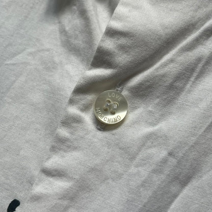 Love Moschino SS19 Dripping Paint Print Button-Up Shirt is a black and white shirt from the Spring/Summer 2019 collection. The upper portion is white, while the lower portion is black. The transition between the two sections features a dripping paint graphic extending downward from both sides into the black area. The button closure uses matching buttons, with white buttons on the white section and black buttons on the black section.
