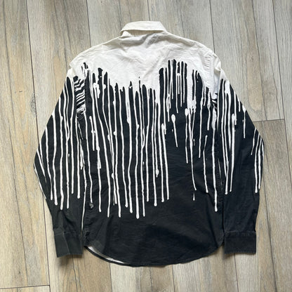 Love Moschino SS19 Dripping Paint Print Button-Up Shirt is a black and white shirt from the Spring/Summer 2019 collection. The upper portion is white, while the lower portion is black. The transition between the two sections features a dripping paint graphic extending downward from both sides into the black area. The button closure uses matching buttons, with white buttons on the white section and black buttons on the black section.
