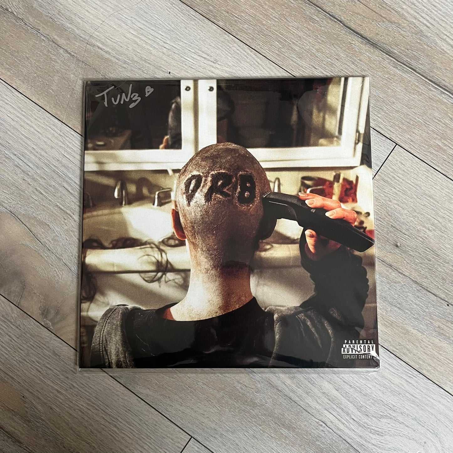Lucki Drgs R Bad* 2026 Signed BRAZY 4 LUCKI Vinyl is a 2xLP release of Lucki’s fourth studio album, originally released on May 15, 2026. The set includes alternative front and back artwork, a widespine jacket, and printed inner sleeves with different graphics for each record. The vinyl records are transparent orange with black smoke effects throughout. The outer jacket features artwork of a girl shaving her head with the DRB logo cut into her hair. This copy is signed by Lucki in the upper left corner with 