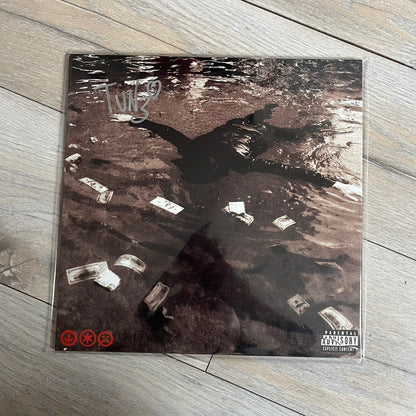 Lucki Dr*gs R Bad 2026 Signed Meet Me @ Viper Room Vinyl is a 2xLP release of Lucki’s fourth studio album, originally released on May 15, 2026. The set includes alternative front and back artwork, a widespine jacket, and printed inner sleeves with different graphics for each record. The vinyl records are transparent black with black smoke effects throughout. The outer jacket features artwork of a person drowning in a pool filled with money. This copy is signed by Lucki in the upper left corner with the insc