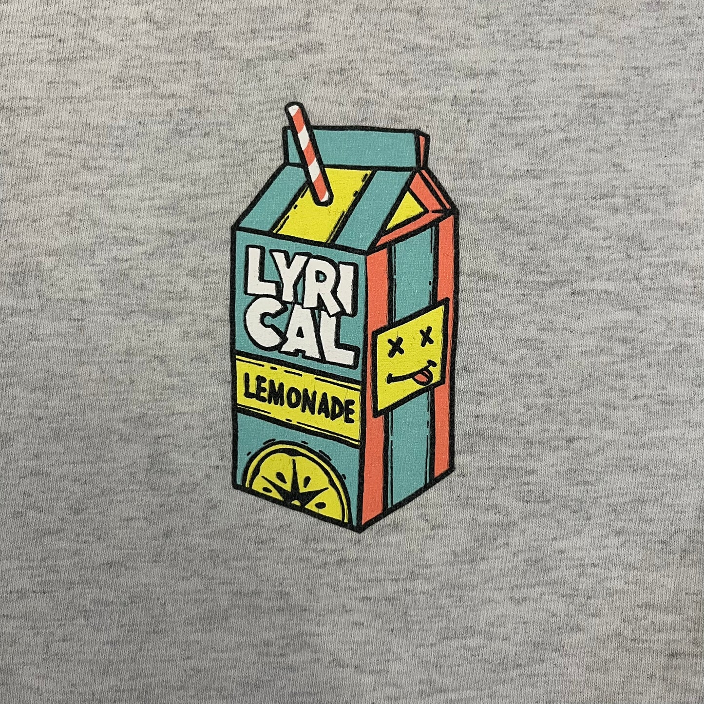 Lyrical Lemonade Everyday Essentials Gray T-Shirt in a gray colorway. Features a small Lyrical Lemonade carton graphic with an xP face printed on the left chest. The back displays a large Lyrical Lemonade logo with text and carton graphics in blue, yellow, and pink, from the Everyday Essentials line.