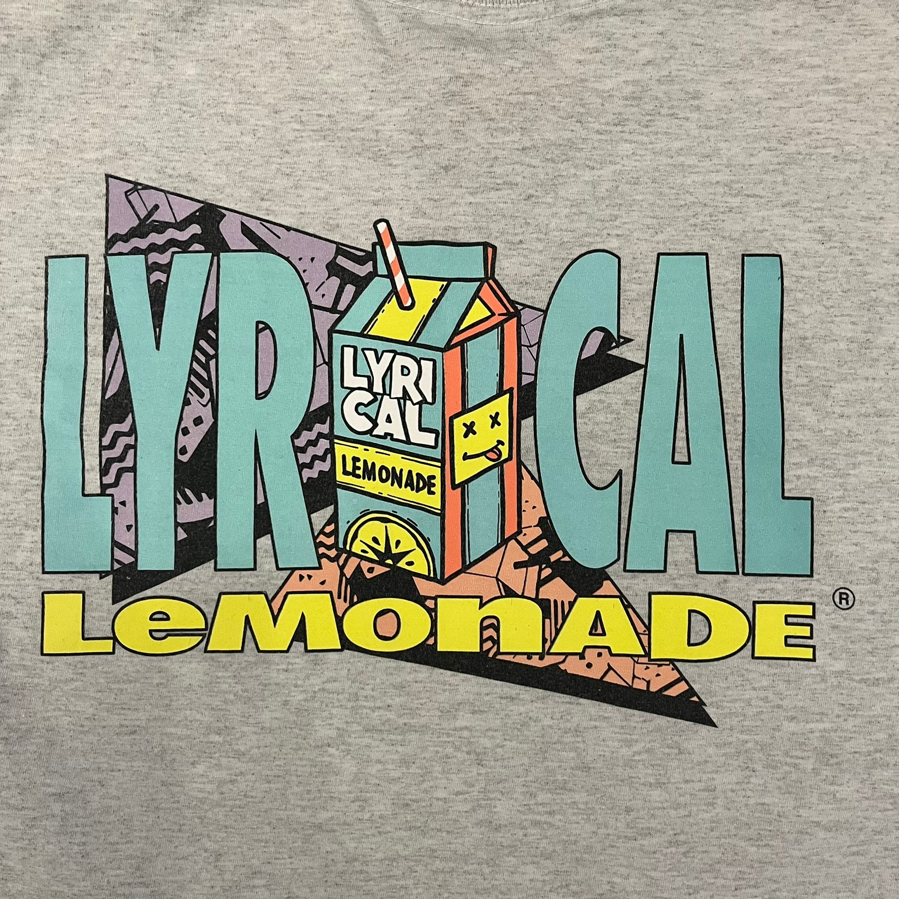 Lyrical Lemonade Everyday Essentials Gray T-Shirt in a gray colorway. Features a small Lyrical Lemonade carton graphic with an xP face printed on the left chest. The back displays a large Lyrical Lemonade logo with text and carton graphics in blue, yellow, and pink, from the Everyday Essentials line.
