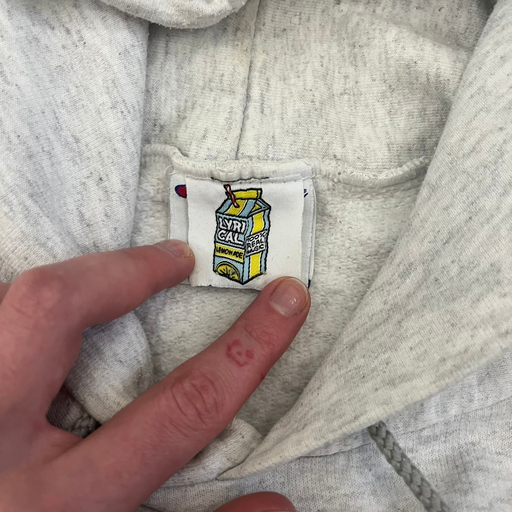 Champion x Lyrical Lemonade Grey Hoodie featuring a triple overlaping lemonade cartoon patch design on the front left chest. Made from a 50/50 cotton-polyester, this medium ash grey hoodie includes a two-ply hood, dyed-to-match drawcord, front pouch pocket, and embroidered Champion logo on the wrist.