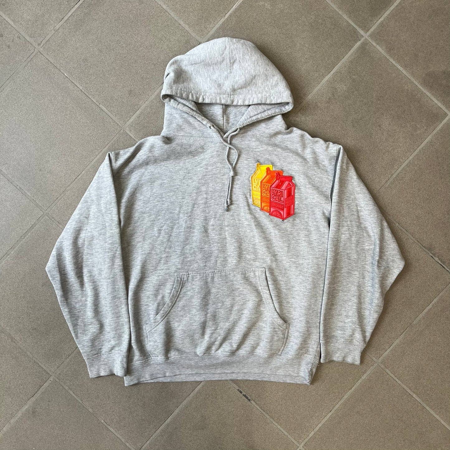 Lyrical Lemonade Triple Patch Gray Hoodie features a gray colorway with a layered triple lemonade box patch design on the left chest in red, yellow, and blue. Made from an 80/20 cotton-polyester blend, the hoodie includes a yellow Lyrical Lemonade neck tag.