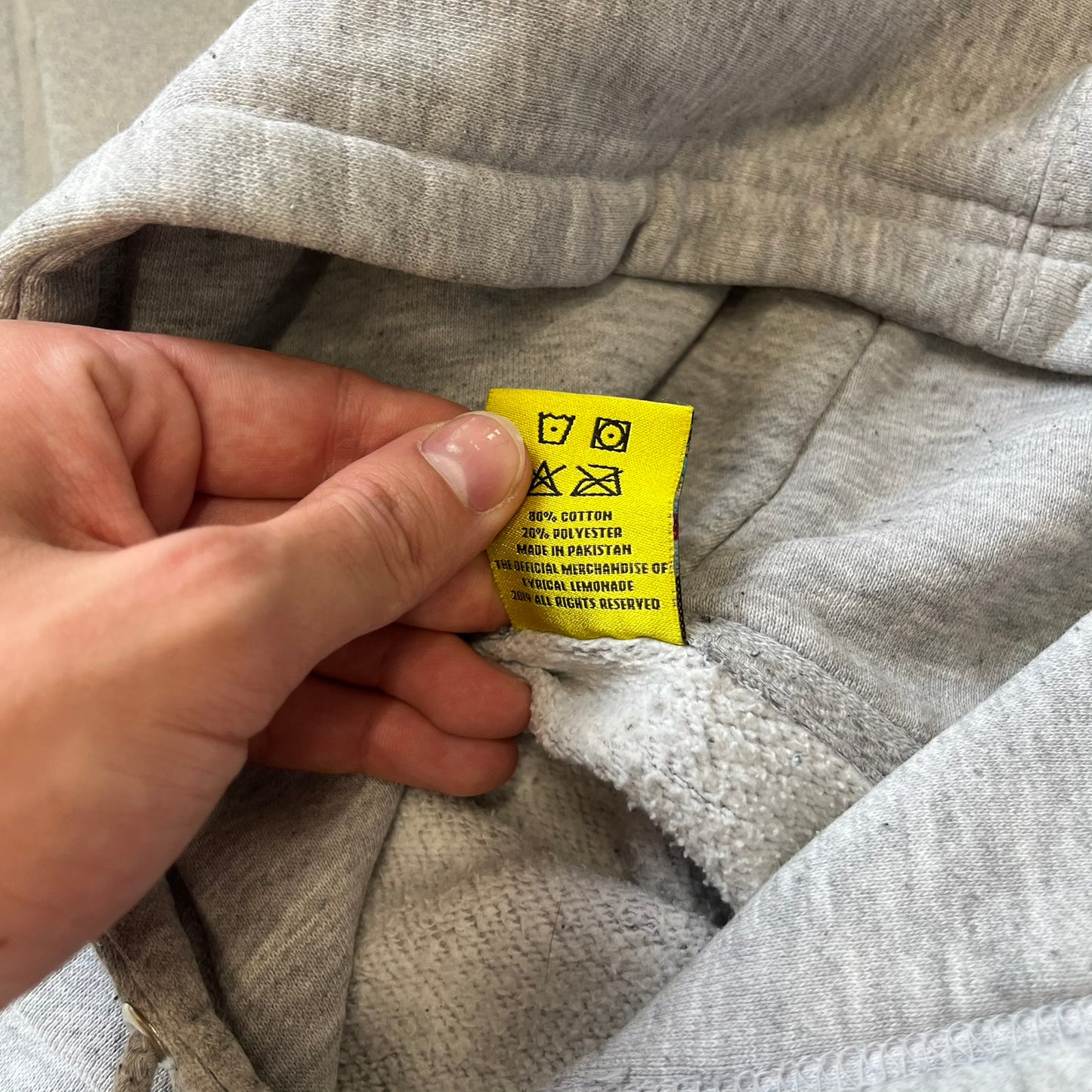 Lyrical Lemonade Triple Patch Gray Hoodie features a gray colorway with a layered triple lemonade box patch design on the left chest in red, yellow, and blue. Made from an 80/20 cotton-polyester blend, the hoodie includes a yellow Lyrical Lemonade neck tag.