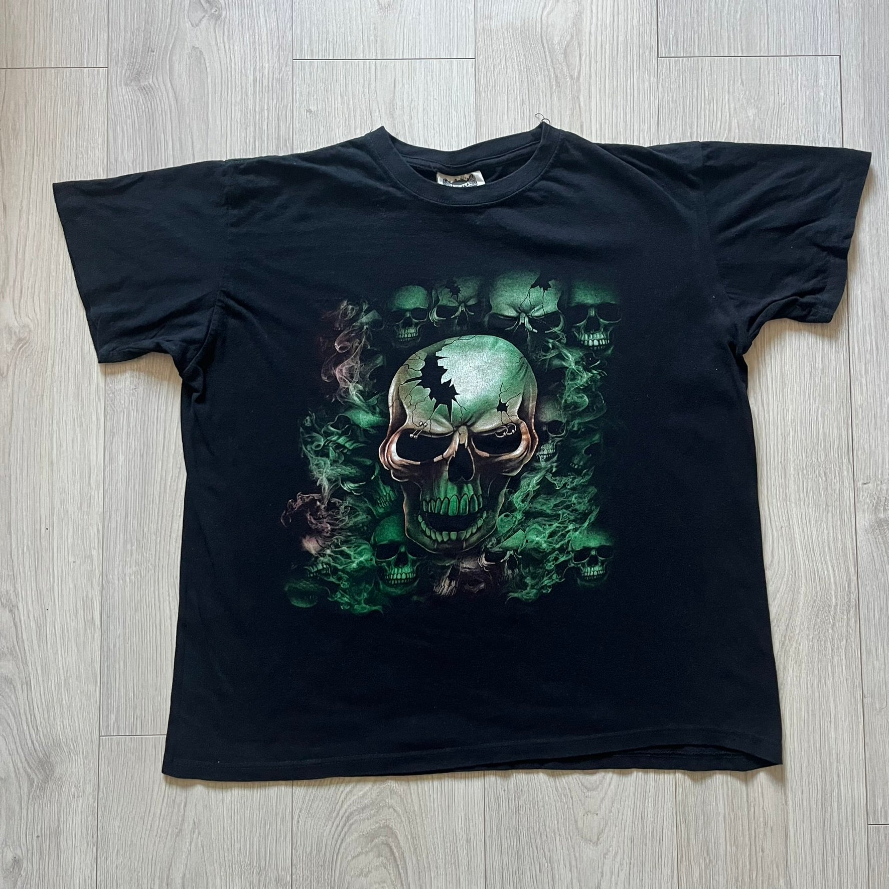 MC5 Boyc Skulls Tee in a wide, boxy-ish fit, crafted from high-quality cotton. The black tee features a large cracked skull with piercings on the front, surrounded by smaller skulls in white and green tones. A bold vintage-inspired graphic piece with strong visual impact.