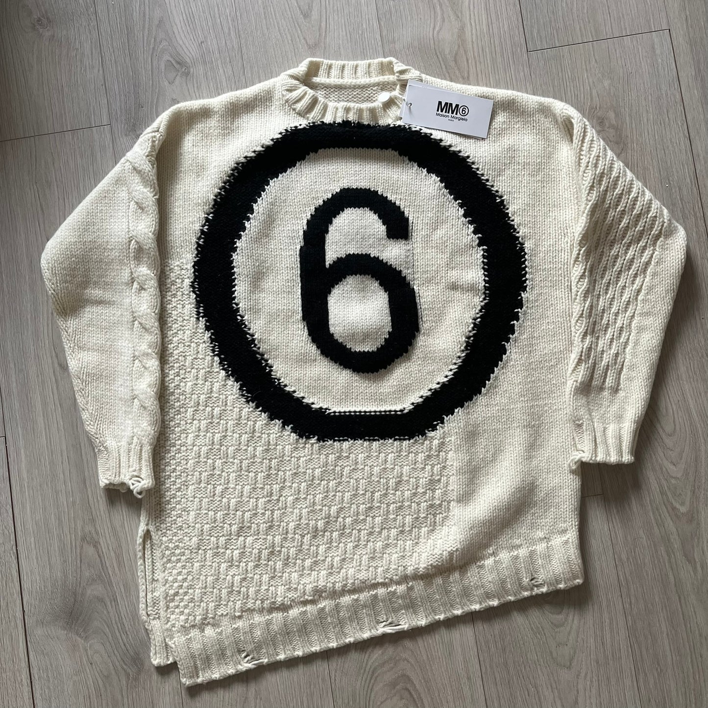White sweater with black circular design and number 6 on a wooden floor