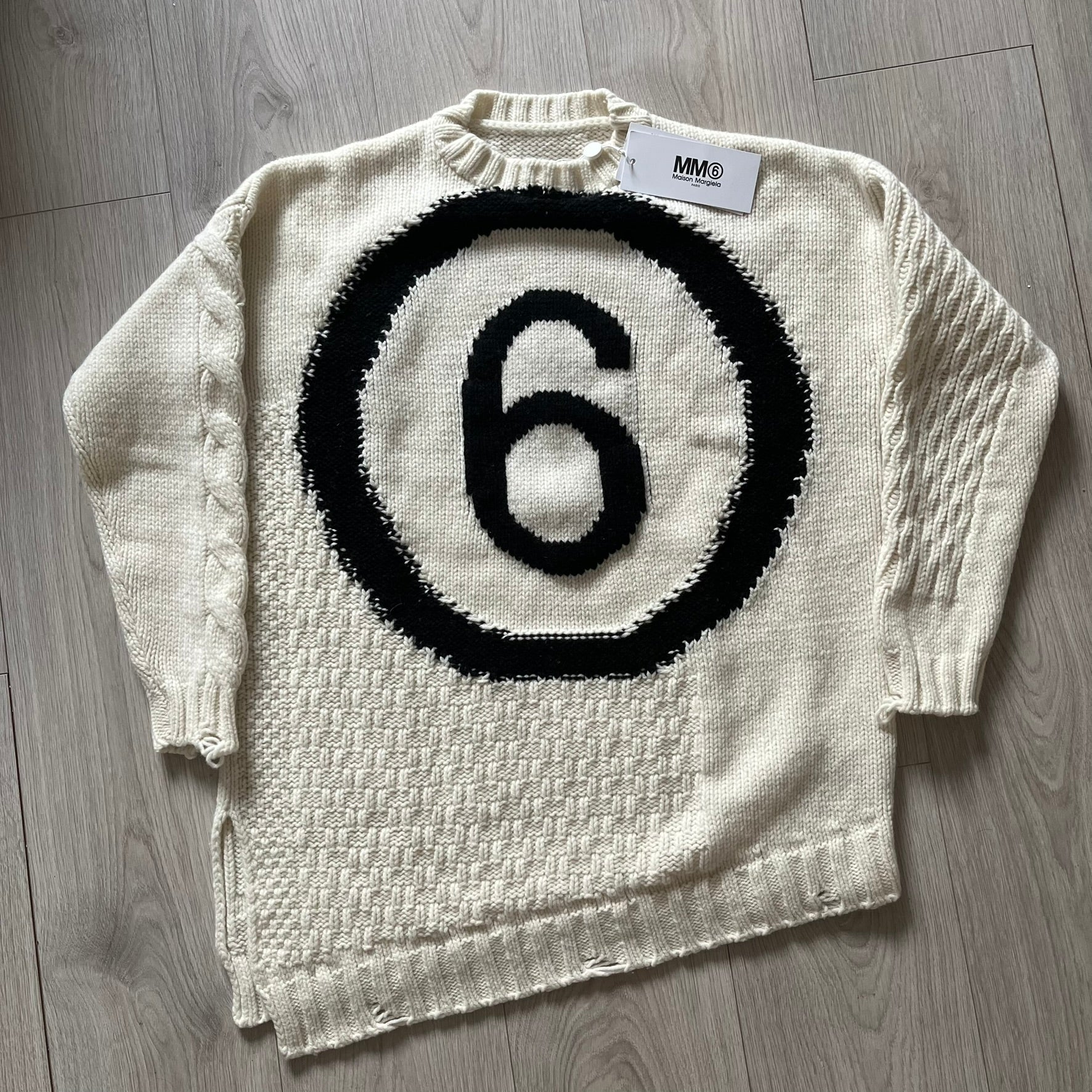 White sweater with black circular design and number 6 on a wooden floor