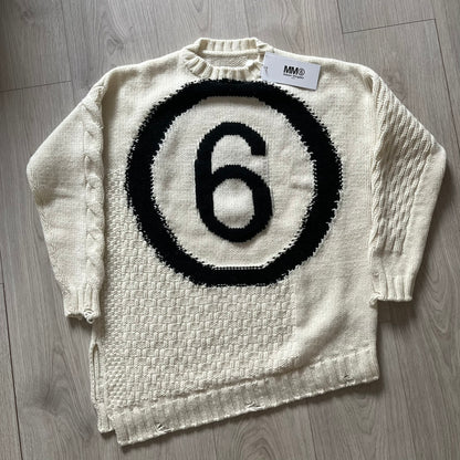 White sweater with black circular design and number 6 on a wooden floor