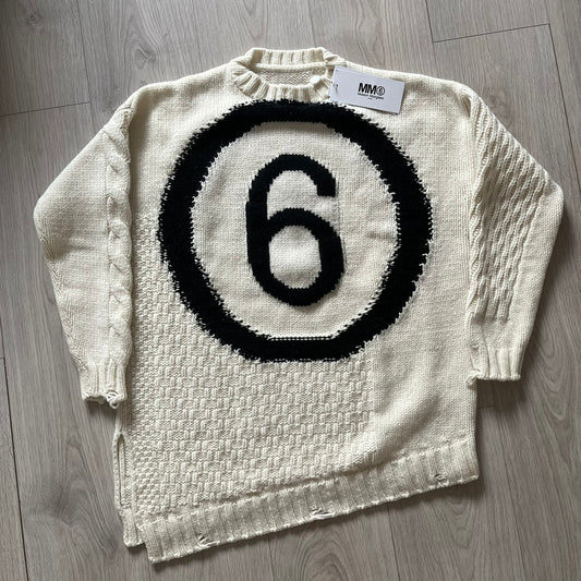 White sweater with black circular design and number 6 on a wooden floor