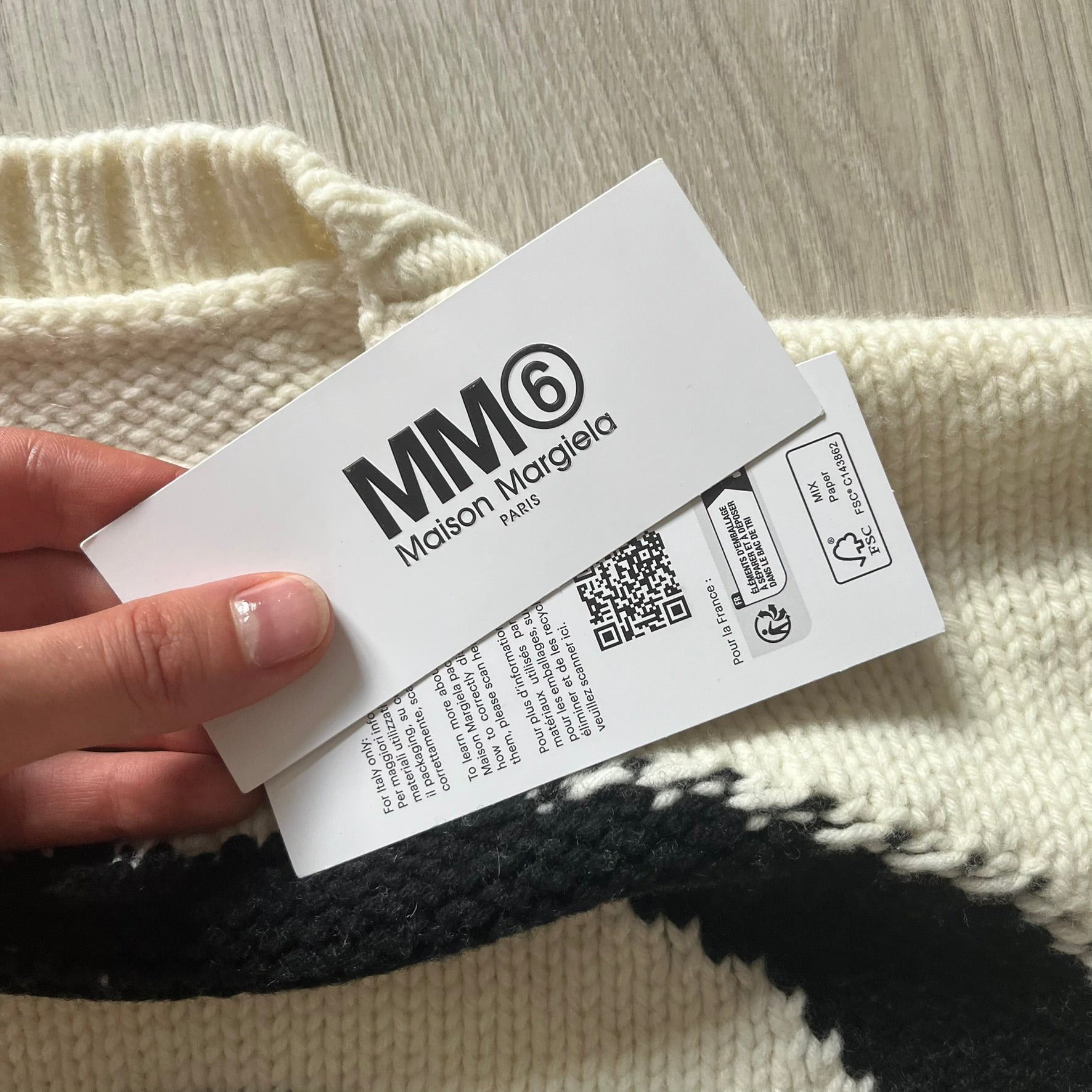 Maison Margiela label held by a hand with a textured fabric background