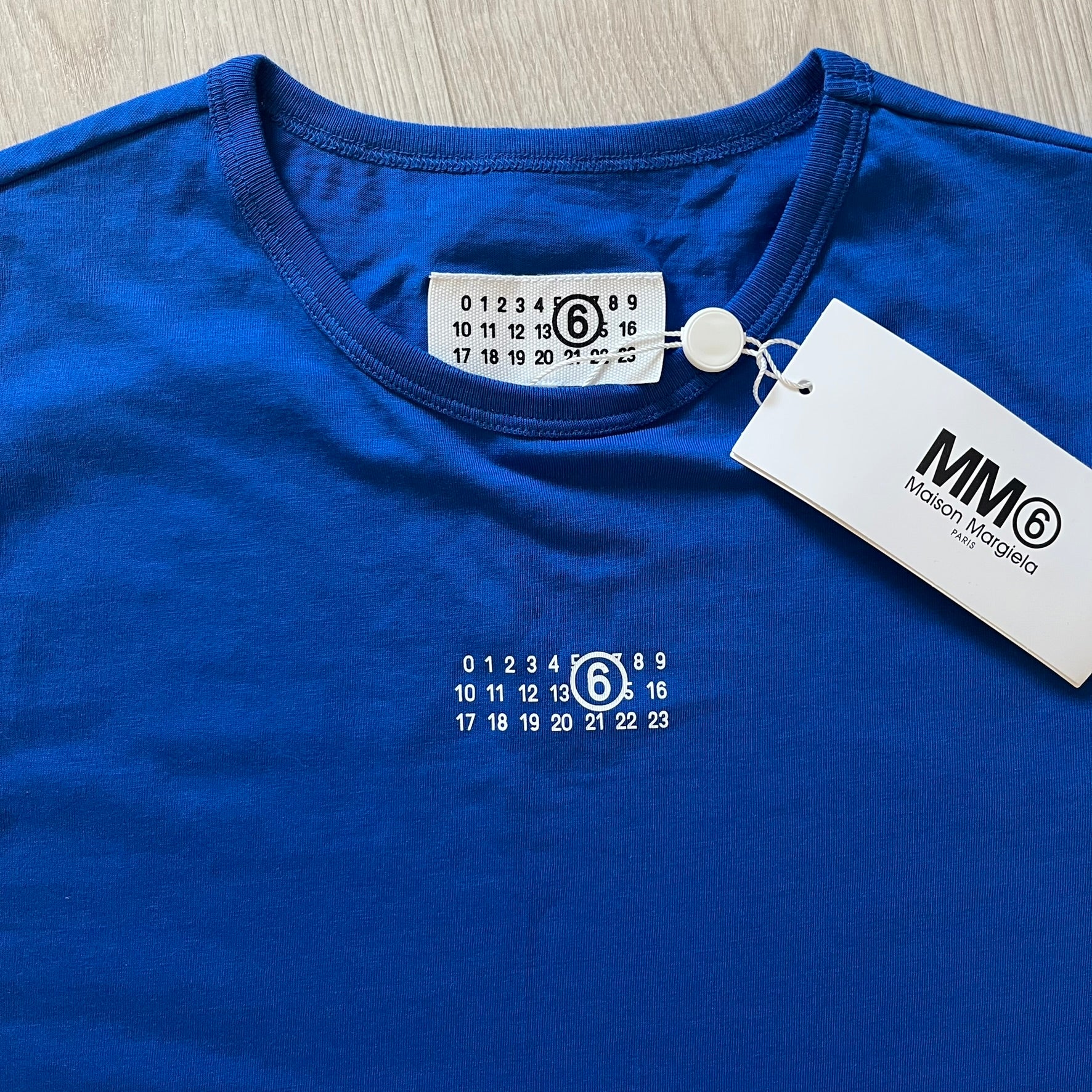 Blue t-shirt with a brand tag and measurement chart on a wooden surface