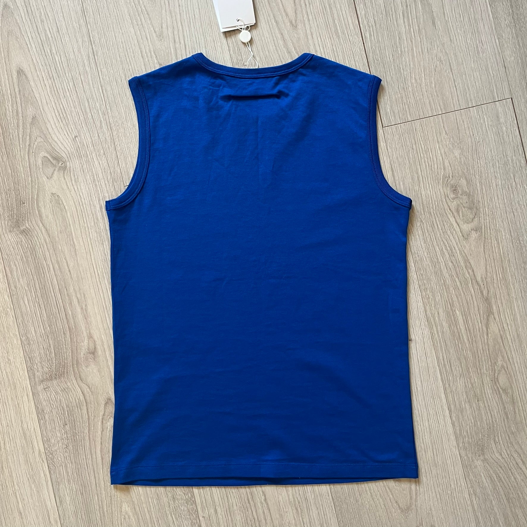 Blue sleeveless shirt on a wooden floor with a tag attached.