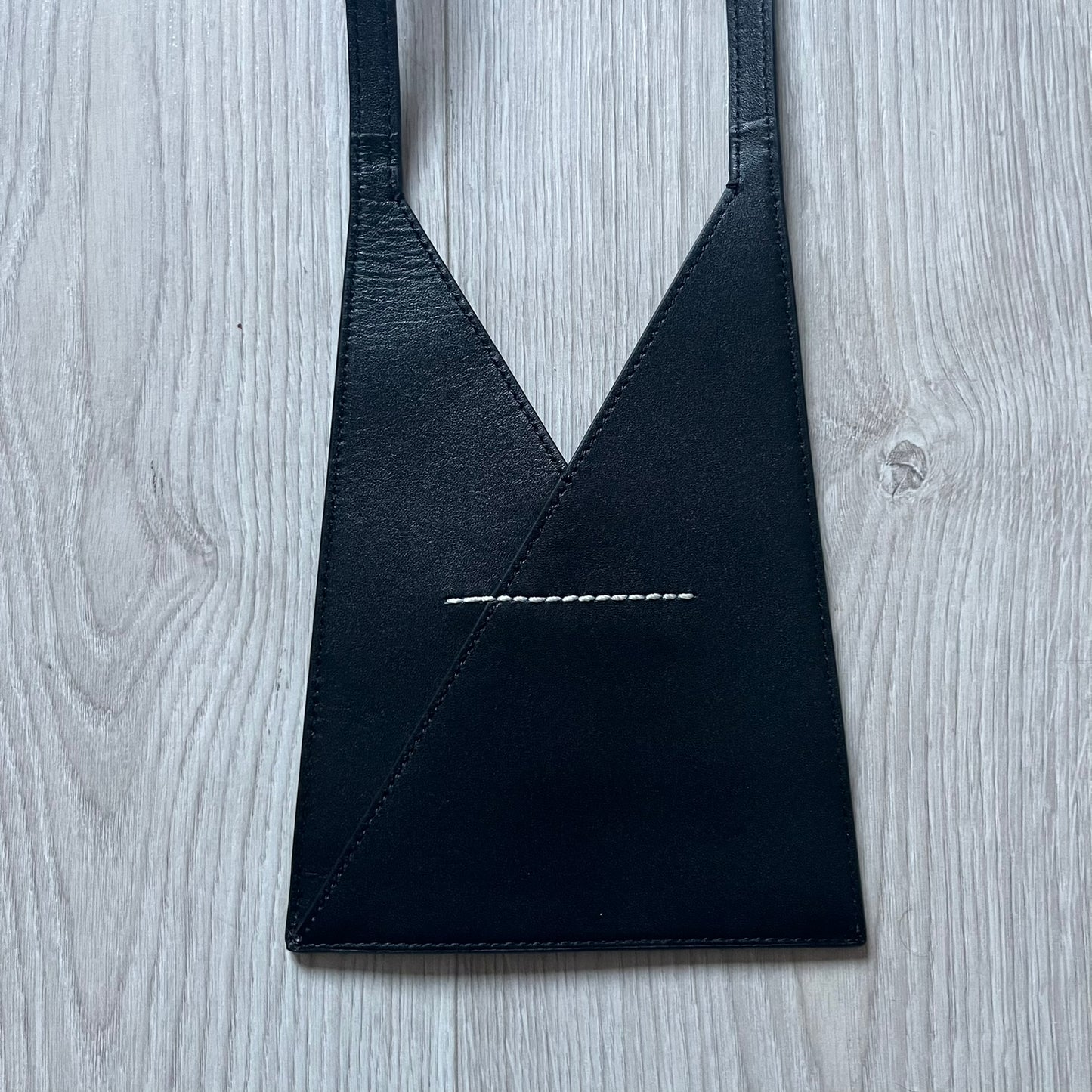 MM6 Maison Margiela Japanese 6 Accordion Phone Bag in black calf leather features a triangular silhouette, tonal stitching, and a single shoulder strap. Compact and structured, this Italian-made bag offers over-the-shoulder or crossbody wear, from the AW22 collection.