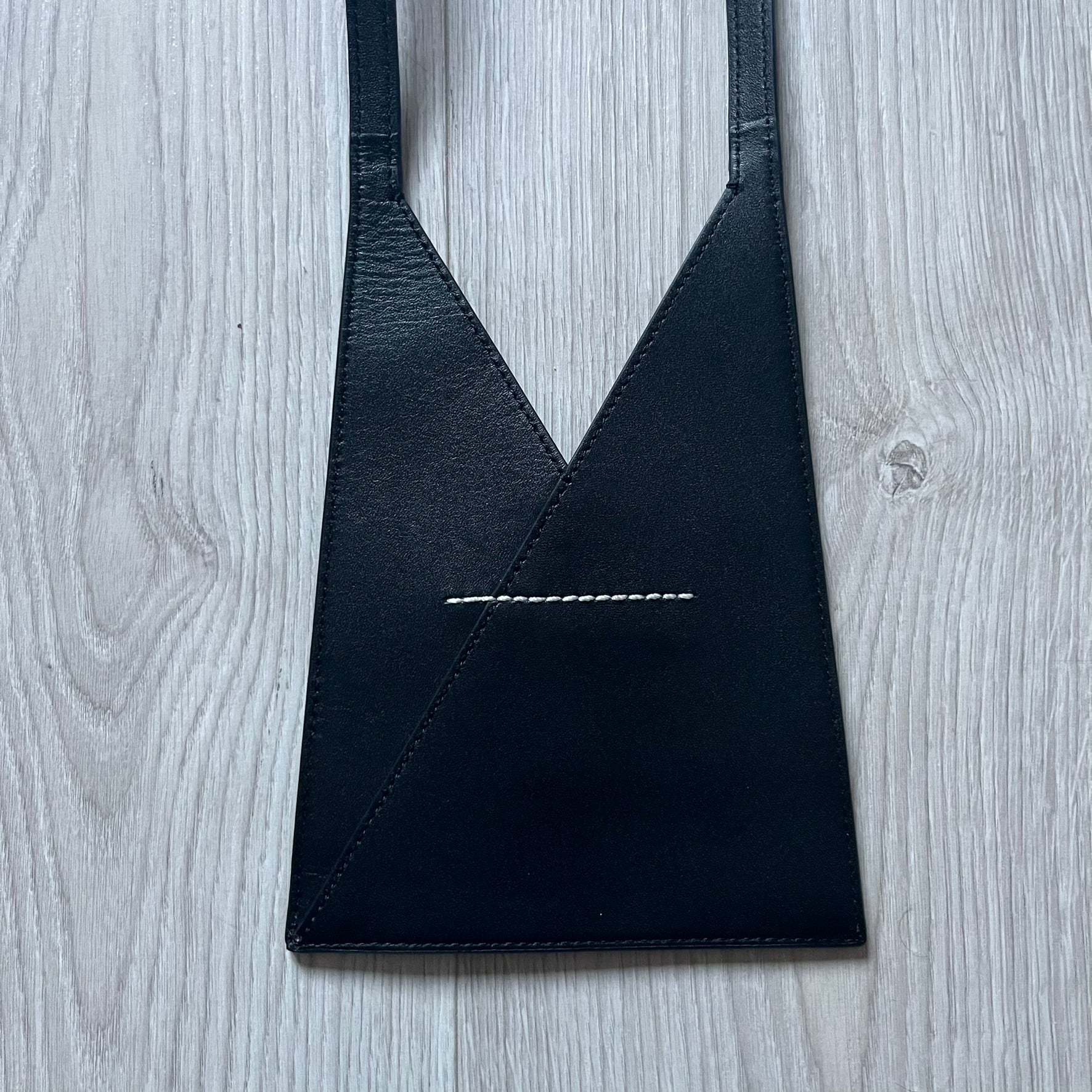 MM6 Maison Margiela Japanese 6 Accordion Phone Bag in black calf leather features a triangular silhouette, tonal stitching, and a single shoulder strap. Compact and structured, this Italian-made bag offers over-the-shoulder or crossbody wear, from the AW22 collection.