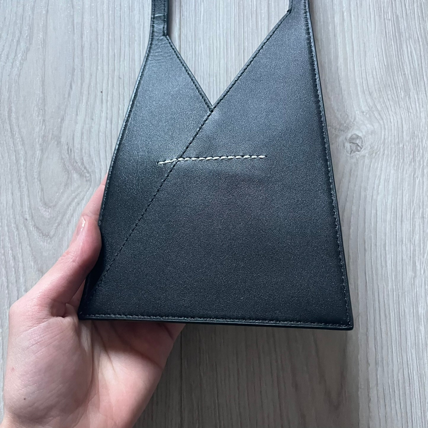 MM6 Maison Margiela Japanese 6 Accordion Phone Bag in black calf leather features a triangular silhouette, tonal stitching, and a single shoulder strap. Compact and structured, this Italian-made bag offers over-the-shoulder or crossbody wear, from the AW22 collection.