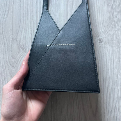 MM6 Maison Margiela Japanese 6 Accordion Phone Bag in black calf leather features a triangular silhouette, tonal stitching, and a single shoulder strap. Compact and structured, this Italian-made bag offers over-the-shoulder or crossbody wear, from the AW22 collection.