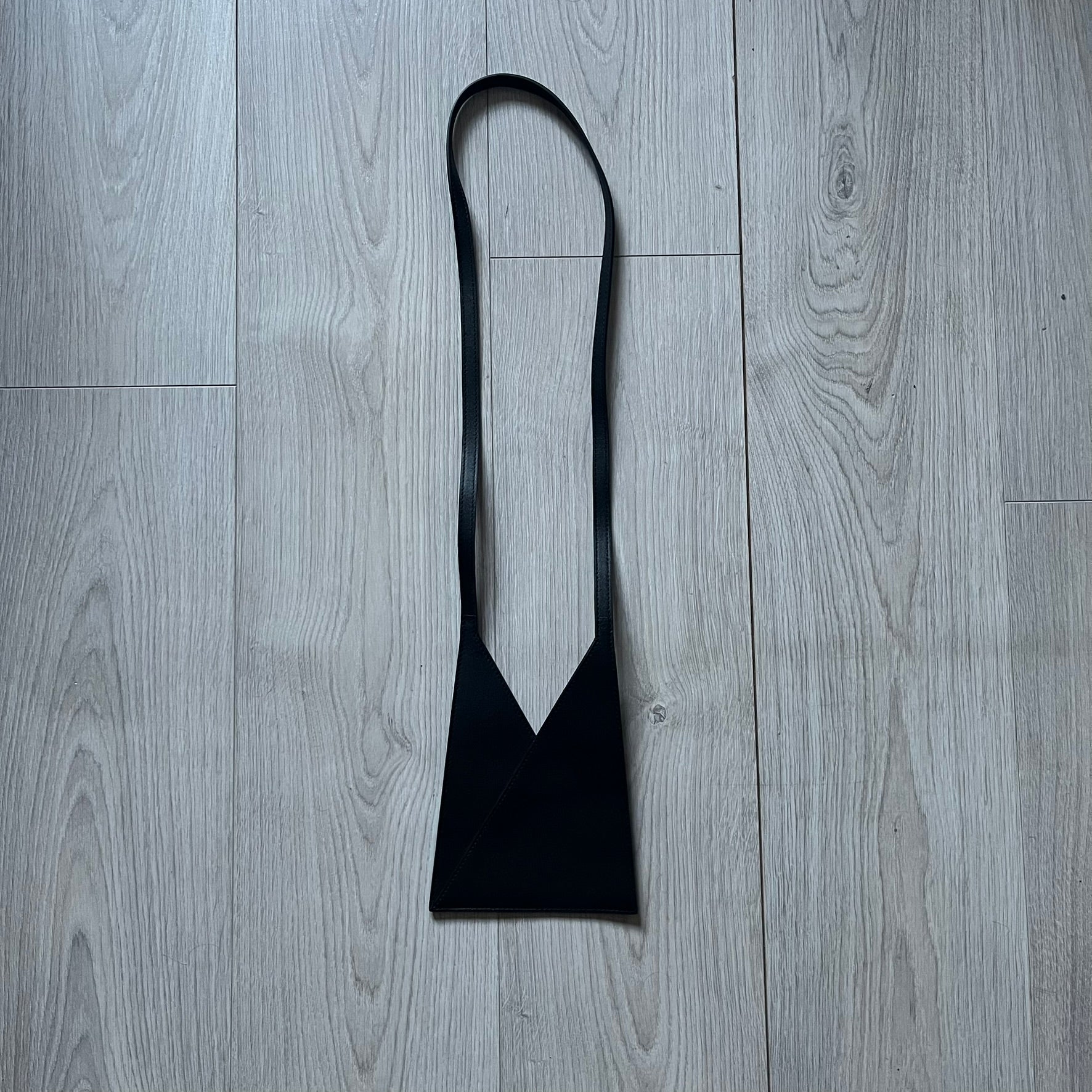 MM6 Maison Margiela Japanese 6 Accordion Phone Bag in black calf leather features a triangular silhouette, tonal stitching, and a single shoulder strap. Compact and structured, this Italian-made bag offers over-the-shoulder or crossbody wear, from the AW22 collection.