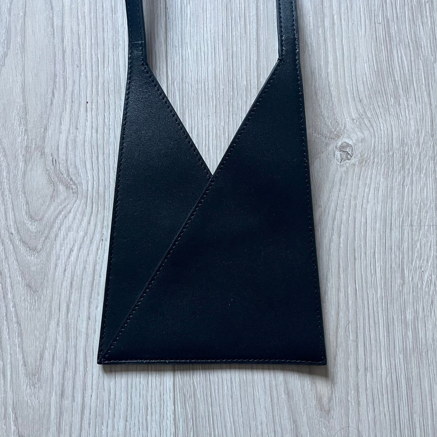 MM6 Maison Margiela Japanese 6 Accordion Phone Bag in black calf leather features a triangular silhouette, tonal stitching, and a single shoulder strap. Compact and structured, this Italian-made bag offers over-the-shoulder or crossbody wear, from the AW22 collection.