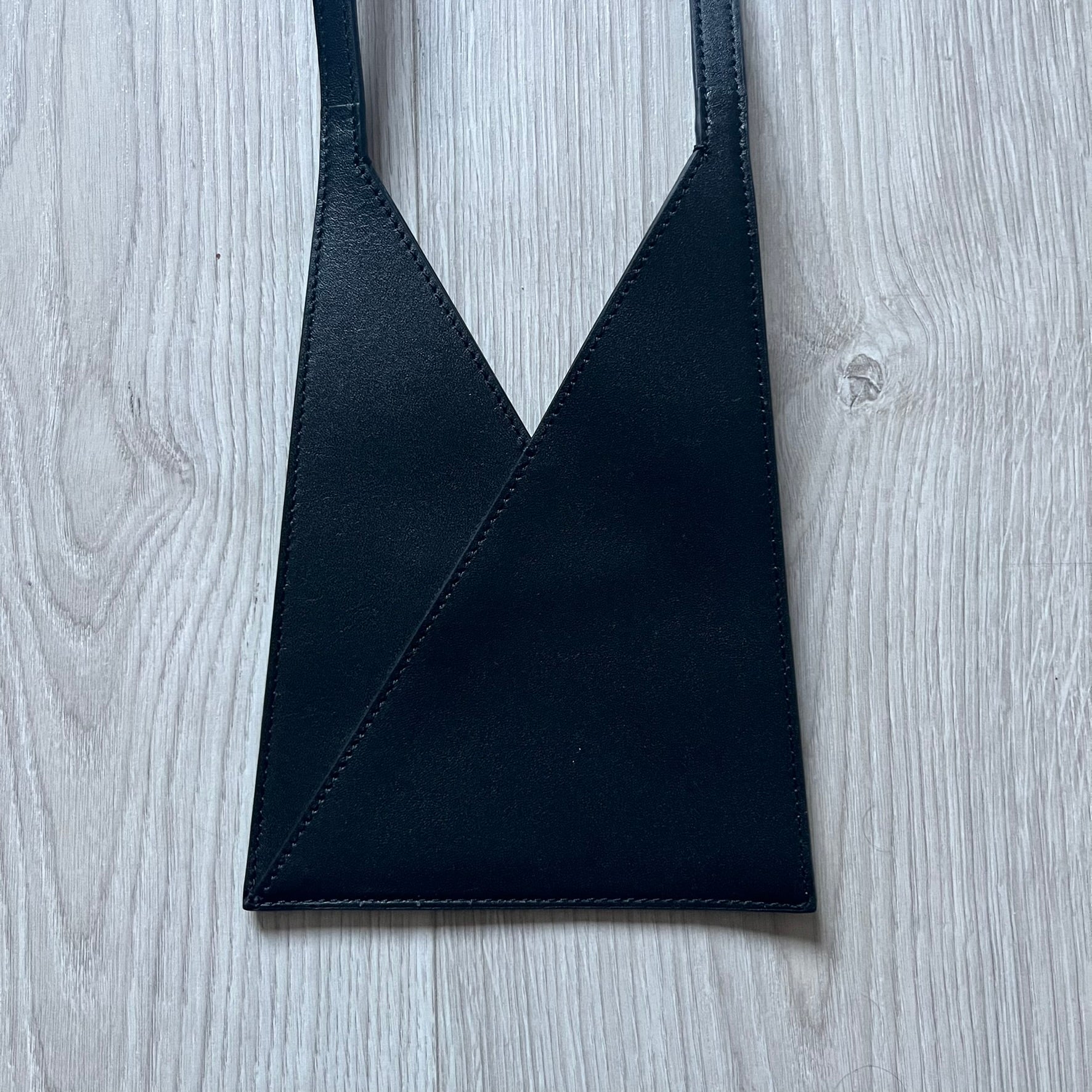 MM6 Maison Margiela Japanese 6 Accordion Phone Bag in black calf leather features a triangular silhouette, tonal stitching, and a single shoulder strap. Compact and structured, this Italian-made bag offers over-the-shoulder or crossbody wear, from the AW22 collection.