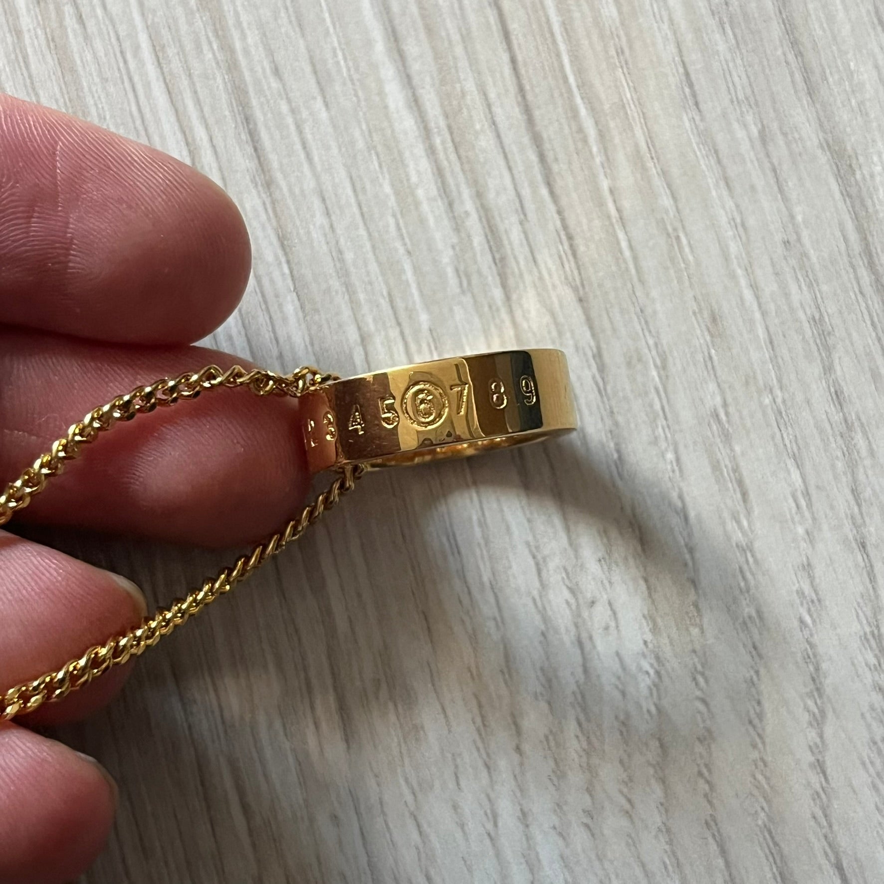 MM6 Maison Margiela gold-tone necklace featuring a polished ring pendant engraved with the brand’s signature number logo. Made in Italy from brass, the design includes a cable-link chain with adjustable length and lobster clasp fastening. A refined accessory that blends subtle branding with timeless elegance.