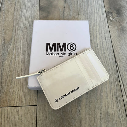 MM6 Maison Margiela White Side Cardholder is a white leather cardholder from MM6 Maison Margiela featuring a horizontal layout with a top zip compartment for coins. The side includes four card slots, while the front displays a mirrored Maison Margiela 6 logo. The item comes with original box and tags.
