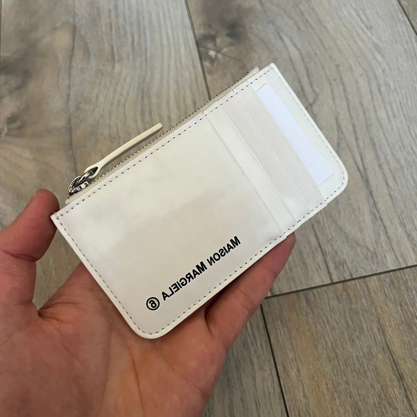 MM6 Maison Margiela White Side Cardholder is a white leather cardholder from MM6 Maison Margiela featuring a horizontal layout with a top zip compartment for coins. The side includes four card slots, while the front displays a mirrored Maison Margiela 6 logo. The item comes with original box and tags.