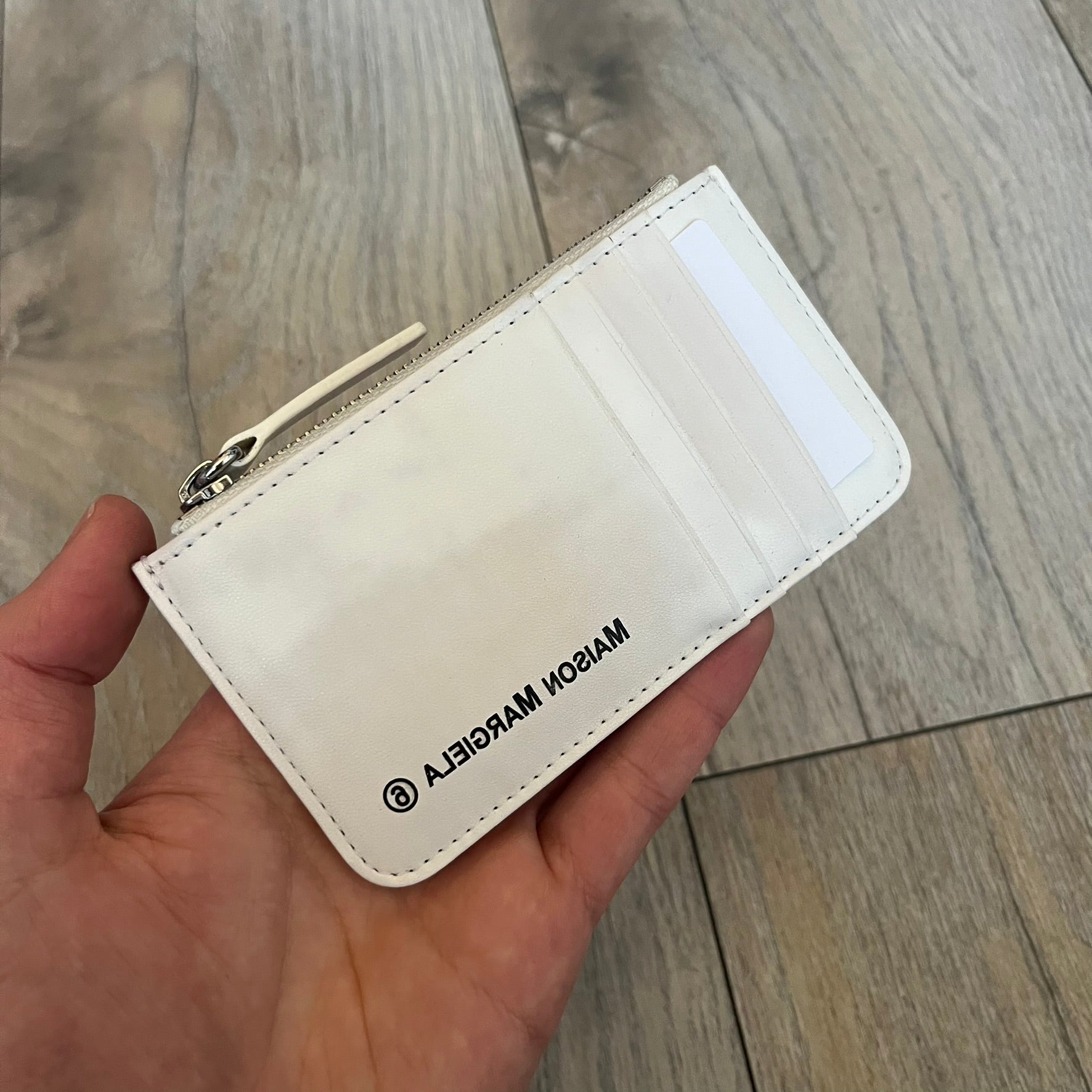 MM6 Maison Margiela White Side Cardholder is a white leather cardholder from MM6 Maison Margiela featuring a horizontal layout with a top zip compartment for coins. The side includes four card slots, while the front displays a mirrored Maison Margiela 6 logo. The item comes with original box and tags.