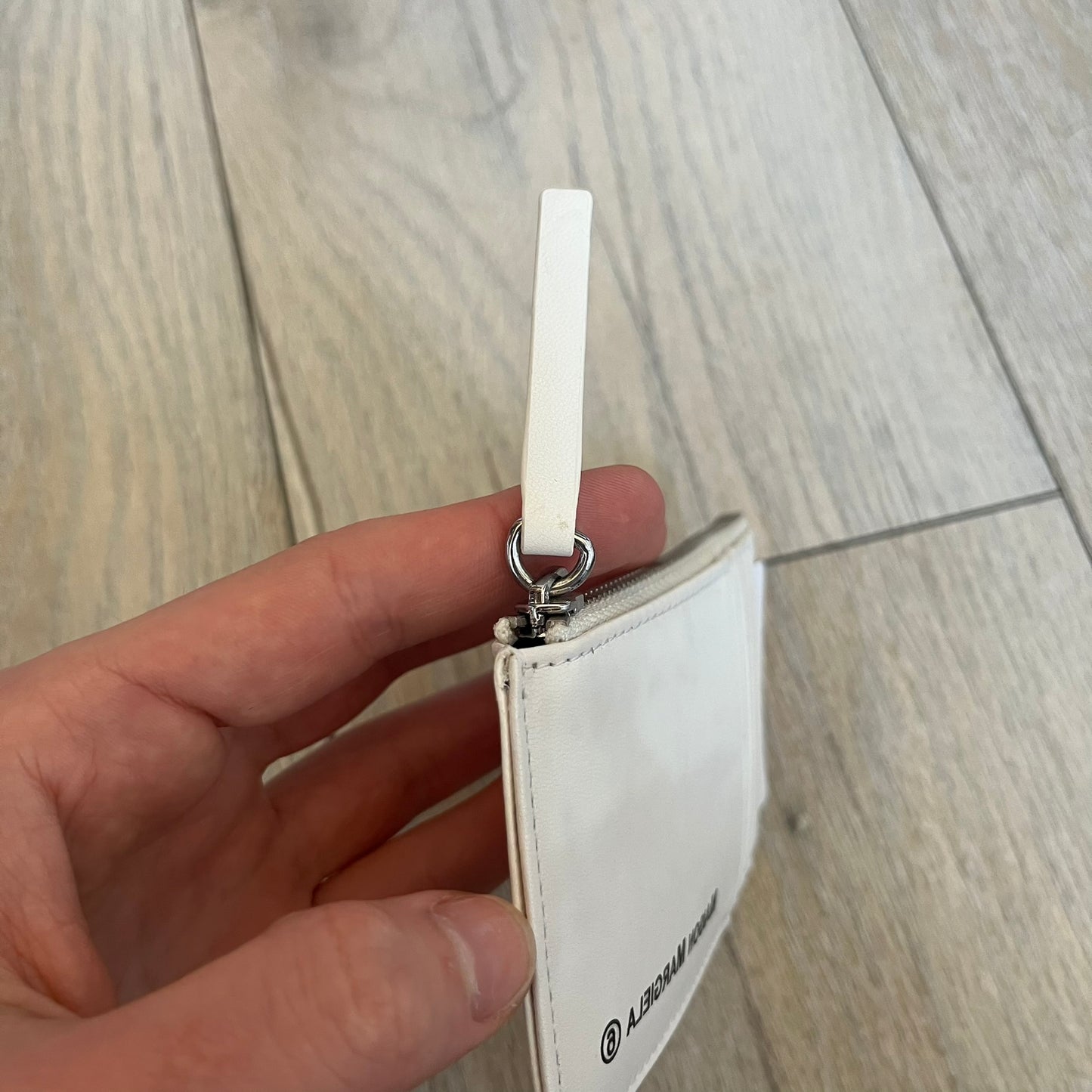 MM6 Maison Margiela White Side Cardholder is a white leather cardholder from MM6 Maison Margiela featuring a horizontal layout with a top zip compartment for coins. The side includes four card slots, while the front displays a mirrored Maison Margiela 6 logo. The item comes with original box and tags.