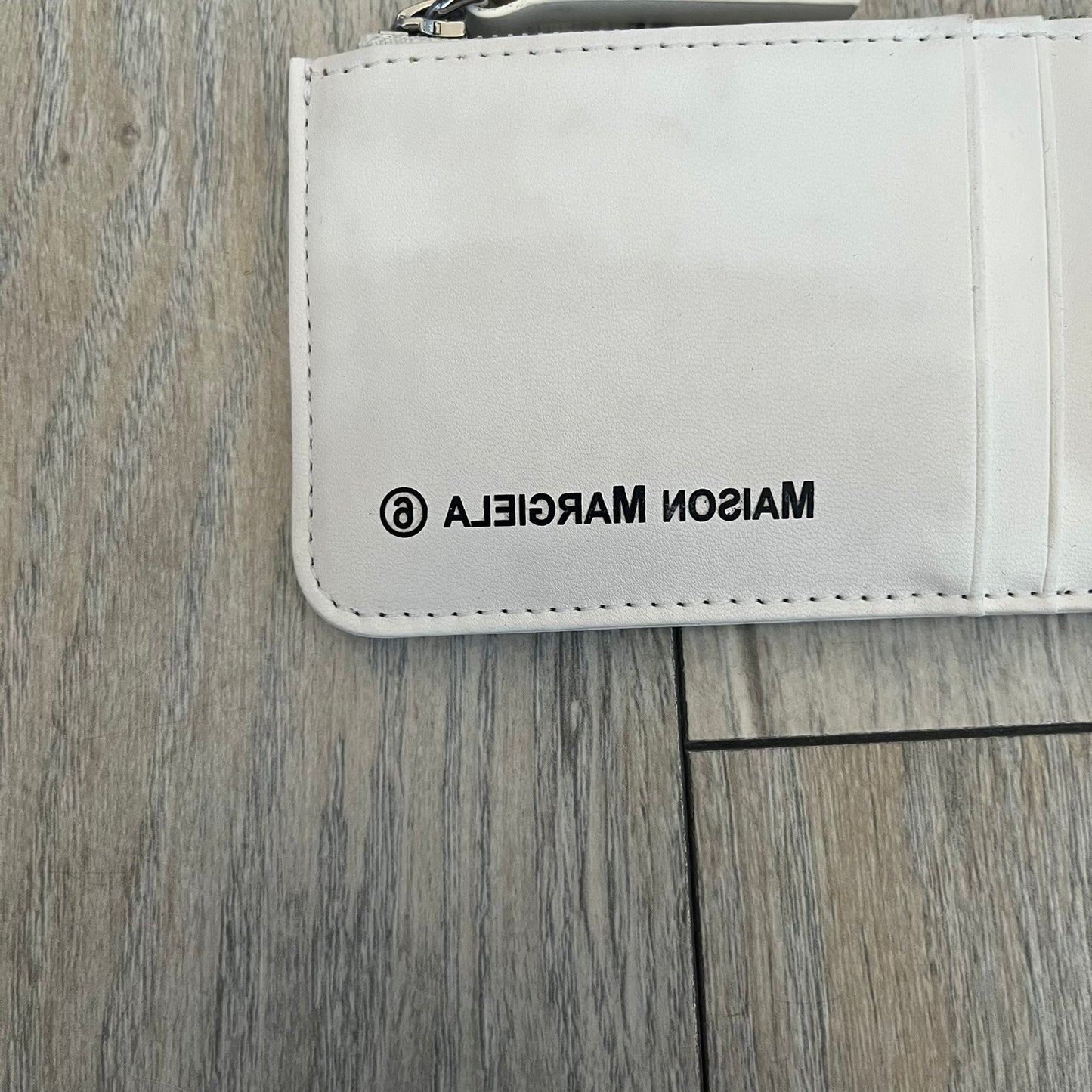 MM6 Maison Margiela White Side Cardholder is a white leather cardholder from MM6 Maison Margiela featuring a horizontal layout with a top zip compartment for coins. The side includes four card slots, while the front displays a mirrored Maison Margiela 6 logo. The item comes with original box and tags.