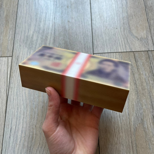 MSCHF Blur ¥5,000 Yen Figure released in October 2023. The collectible object is designed as a stack of ¥5,000 Japanese yen banknotes with a blurred sculptural effect across the entire surface. The piece recreates the appearance of a money stack while distorting the printed details, giving it a block-like form resembling a stylized or game-like currency bundle.