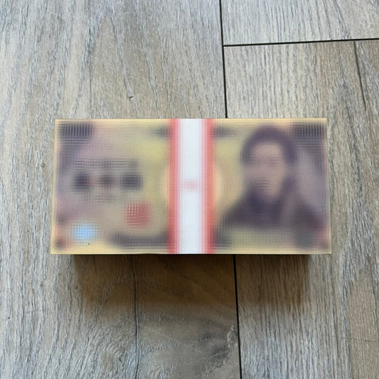 MSCHF Blur ¥5,000 Yen Figure released in October 2023. The collectible object is designed as a stack of ¥5,000 Japanese yen banknotes with a blurred sculptural effect across the entire surface. The piece recreates the appearance of a money stack while distorting the printed details, giving it a block-like form resembling a stylized or game-like currency bundle.