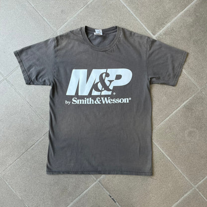 M&P by Smith & Wesson Gray Tee features a washed grey finish with a large M&P logo printed across the front and smaller "by Smith & Wesson" text underneath. Made from 100% cotton on a Gildan blank