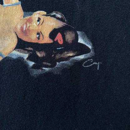 Mafia 2 Smoking Woman 2010 Black Promo Tee features a black T-shirt made on a Stedman blank. The front has a large graphic of a woman lying down while smoking a cigarette and holding dynamite in the other hand. A white and red Mafia II logo is printed above the graphic.
