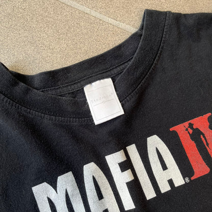 Mafia 2 Smoking Woman 2010 Black Promo Tee features a black T-shirt made on a Stedman blank. The front has a large graphic of a woman lying down while smoking a cigarette and holding dynamite in the other hand. A white and red Mafia II logo is printed above the graphic.
