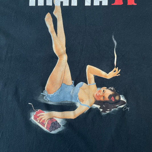 Mafia 2 Smoking Woman 2010 Black Promo Tee features a black T-shirt made on a SG blank. The front has a large graphic of a woman lying down while smoking a cigarette and holding dynamite in the other hand. A white and red Mafia II logo is printed above the graphic.
