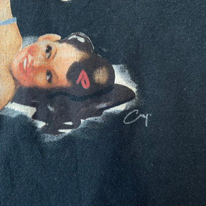 Mafia 2 Smoking Woman 2010 Black Promo Tee features a black T-shirt made on a SG blank. The front has a large graphic of a woman lying down while smoking a cigarette and holding dynamite in the other hand. A white and red Mafia II logo is printed above the graphic.
