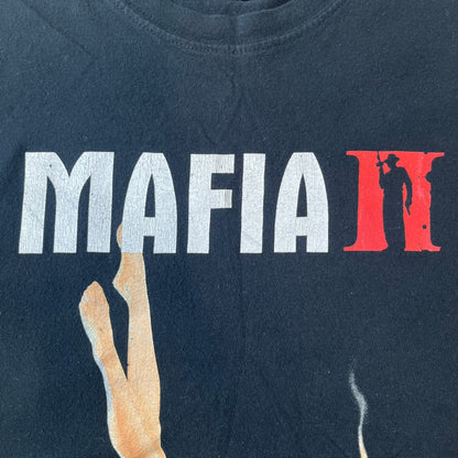 Mafia 2 Smoking Woman 2010 Black Promo Tee features a black T-shirt made on a SG blank. The front has a large graphic of a woman lying down while smoking a cigarette and holding dynamite in the other hand. A white and red Mafia II logo is printed above the graphic.
