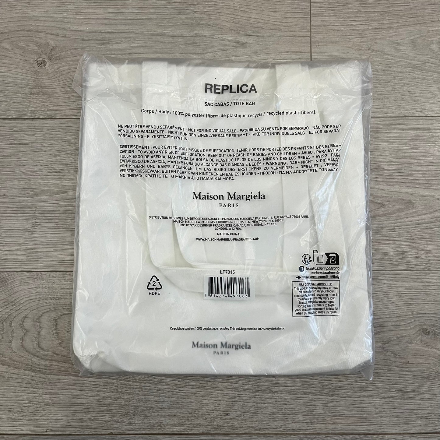 Maison Margiela Replica Tote Bag in off-white with a textured finish inspired by natural jute. Features “Replica” fragrances patch on one side, an interior slip pocket, and small “Maison Margiela Paris” text on the other side. Made in Paris, versatile for daily errands, work, or casual outings.