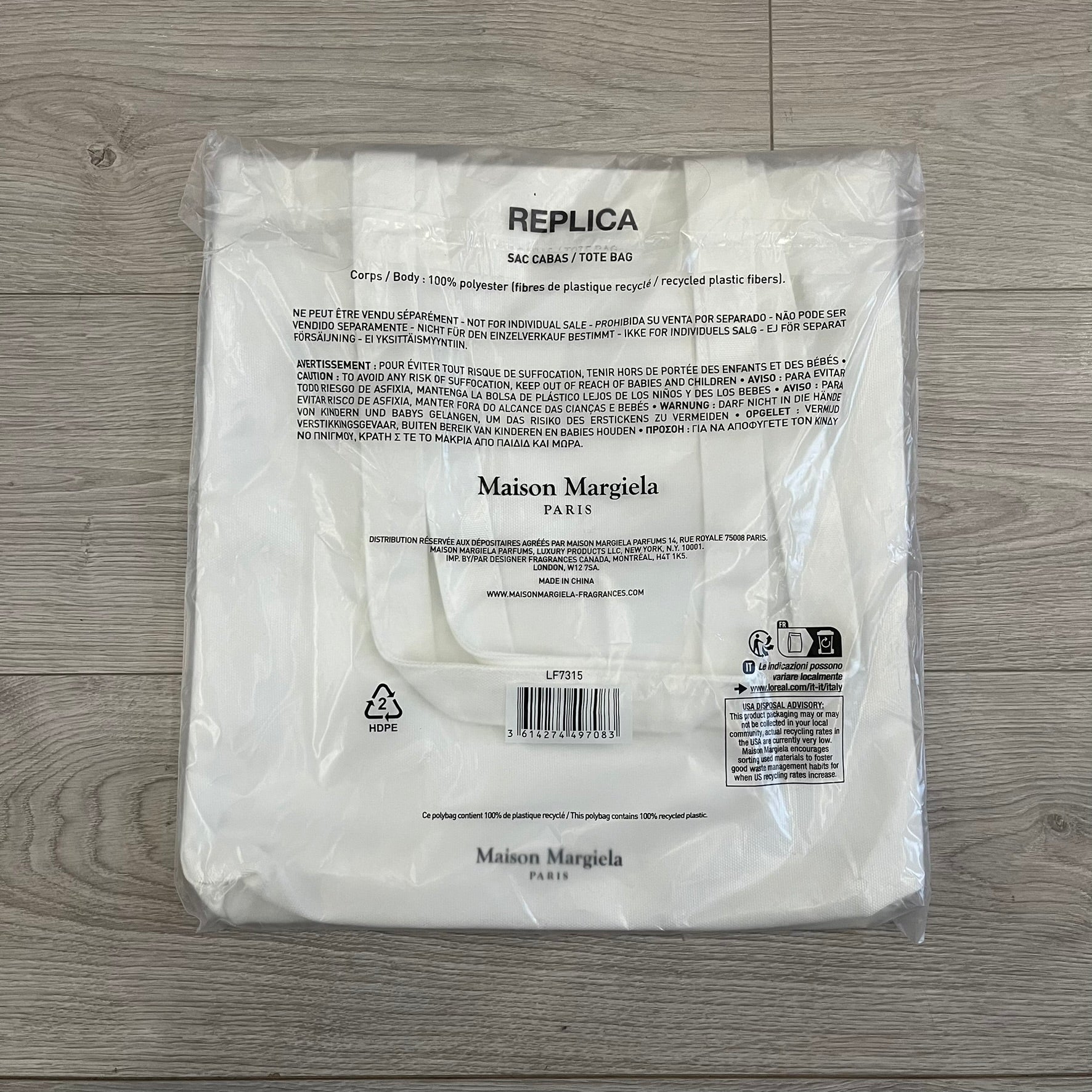 Maison Margiela Replica Tote Bag in off-white with a textured finish inspired by natural jute. Features “Replica” fragrances patch on one side, an interior slip pocket, and small “Maison Margiela Paris” text on the other side. Made in Paris, versatile for daily errands, work, or casual outings.