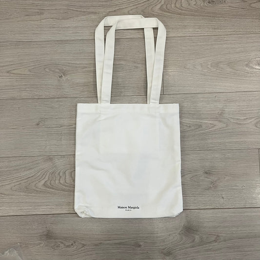 Maison Margiela Replica Tote Bag in off-white with a textured finish inspired by natural jute. Features “Replica” fragrances patch on one side, an interior slip pocket, and small “Maison Margiela Paris” text on the other side. Made in Paris, versatile for daily errands, work, or casual outings.